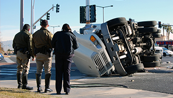 Law enforcement officers observing an overturned truck at a traffic intersection.