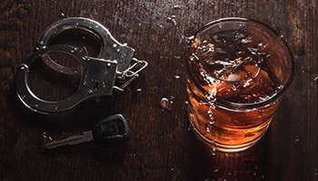 Handcuffs and a glass of whiskey with ice on a dark wooden surface.